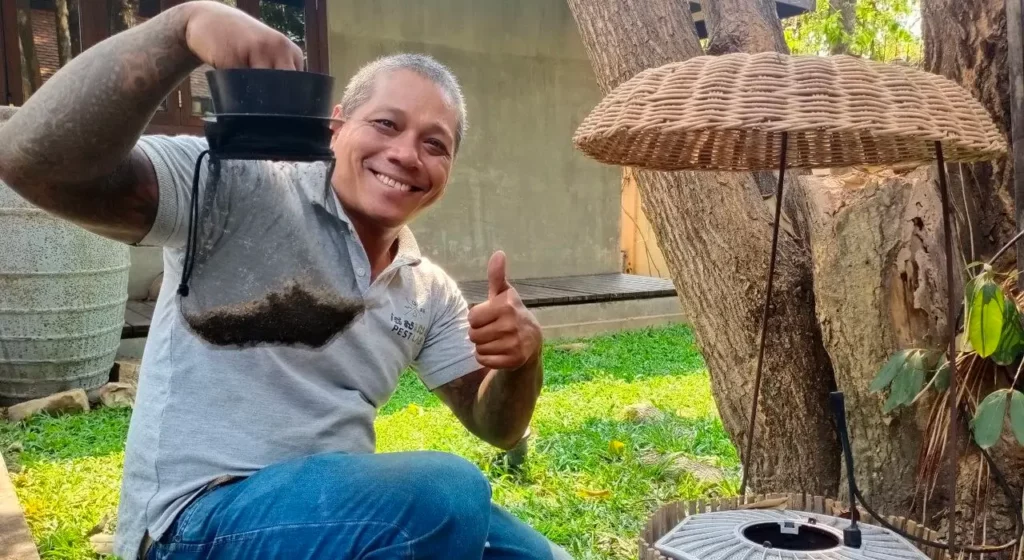 PestLab Laos technician installing outdoor insect trap and showing captured flies in garden environment